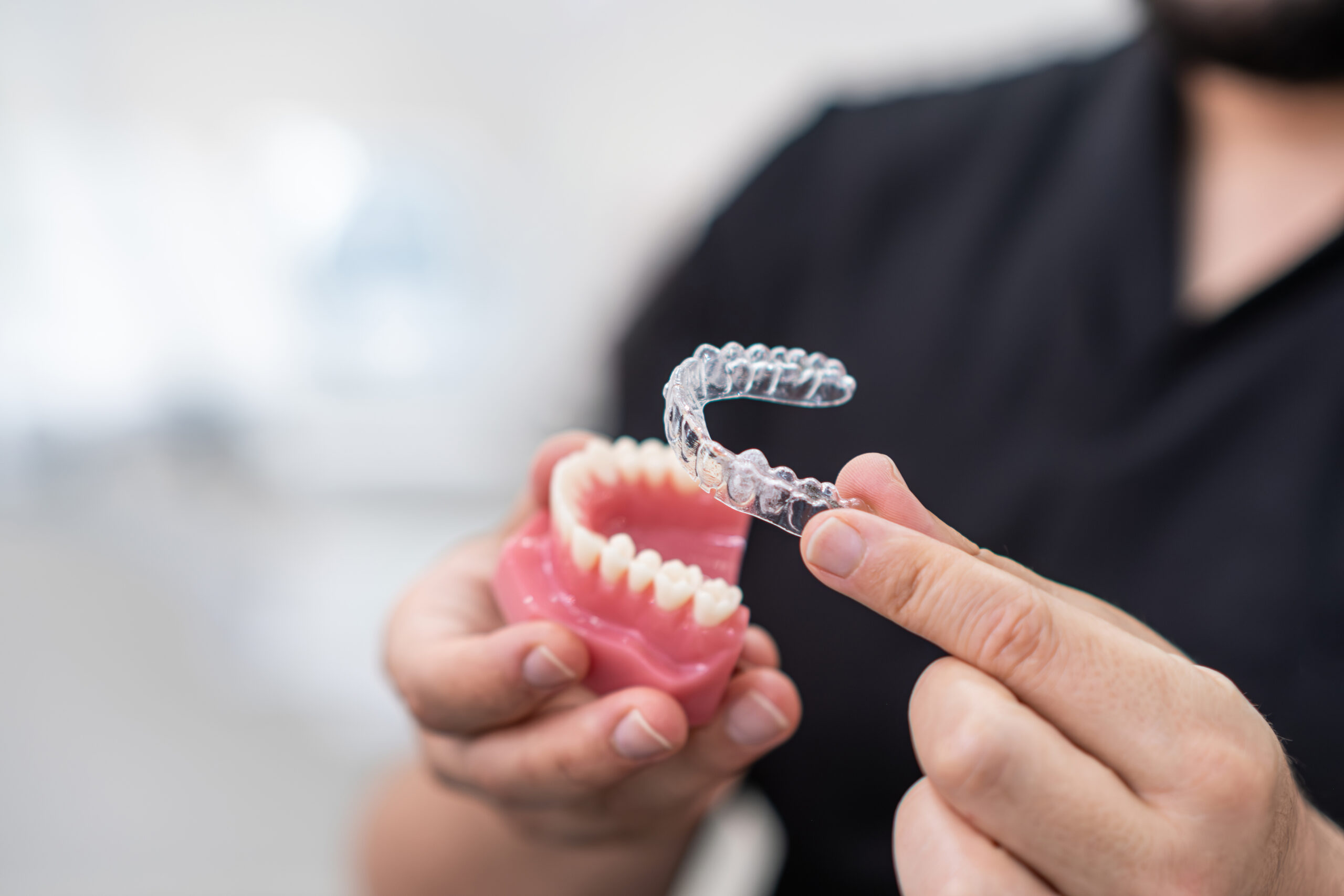 Dentist installing clear aligners on plastic lower human jaw model to show simple and effective device in stomatology clinic specialist performing teeth improvement